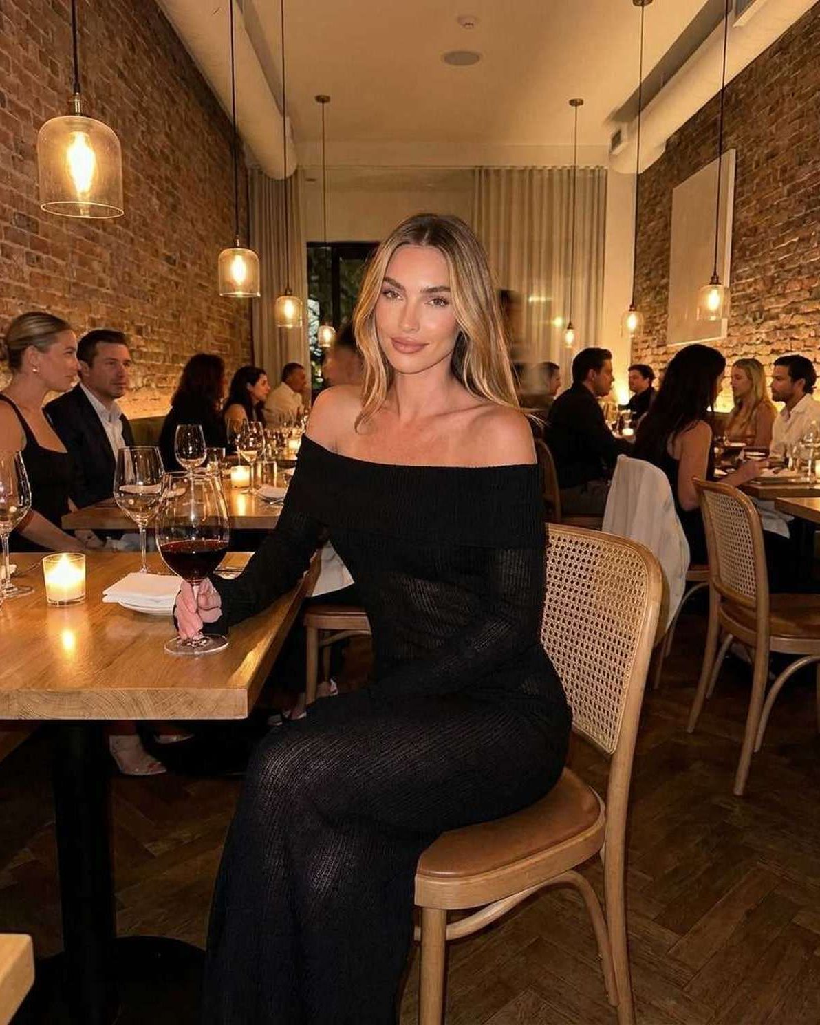 Seren Maxi Dress worn by a woman in a black off-shoulder style at a restaurant, showcasing a sleek silhouette.