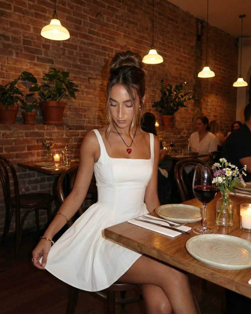 Elegant woman wearing Serena Mini Dress by Lauven in a cozy restaurant with a brick wall backdrop.