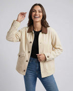 A woman wearing the Sienna Jacket by Lauven, an oversized cream jacket with a brown lapel collar, smiling.