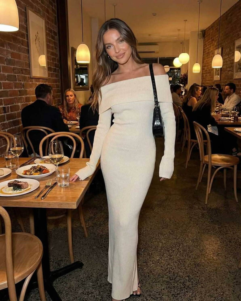 Sienna Maxi Dress by Lauven worn by a model in a restaurant, featuring an ivory off shoulder design and ribbed knit fabric.