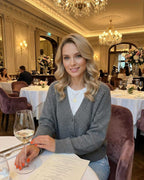 Woman wearing a Slate Cardigan by Lauven, seated at an elegant restaurant table with a glass of wine.