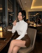 Umbria Mini Skirt worn by a woman enjoying a drink in a stylish restaurant, featuring a high-waisted A-line design.