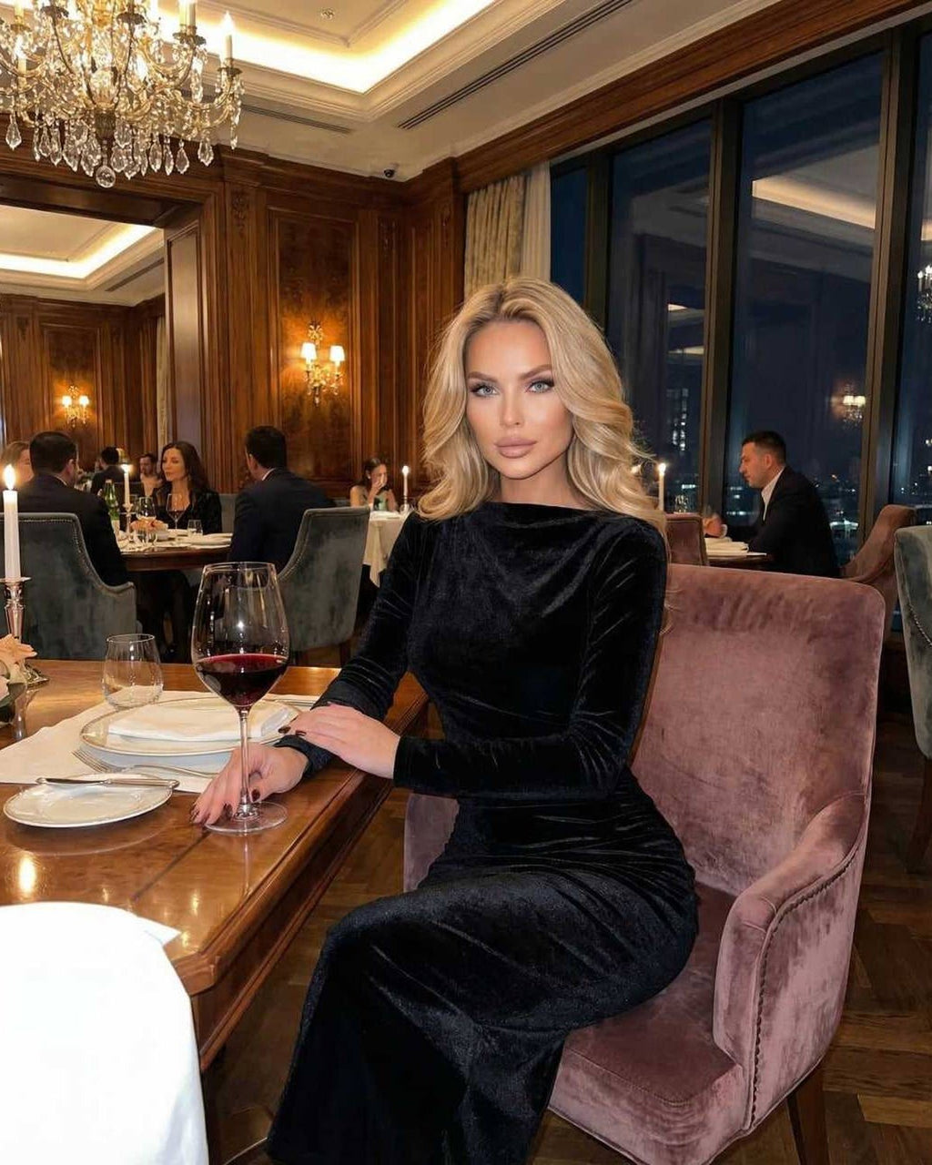 Model wearing the Vega Midi Dress by Lauven, an elegant black velvet long sleeve dress at a sophisticated dinner setting.