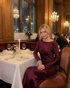 Vesper Maxi Dress by Lauven in rich burgundy satin worn at an elegant dinner setting.