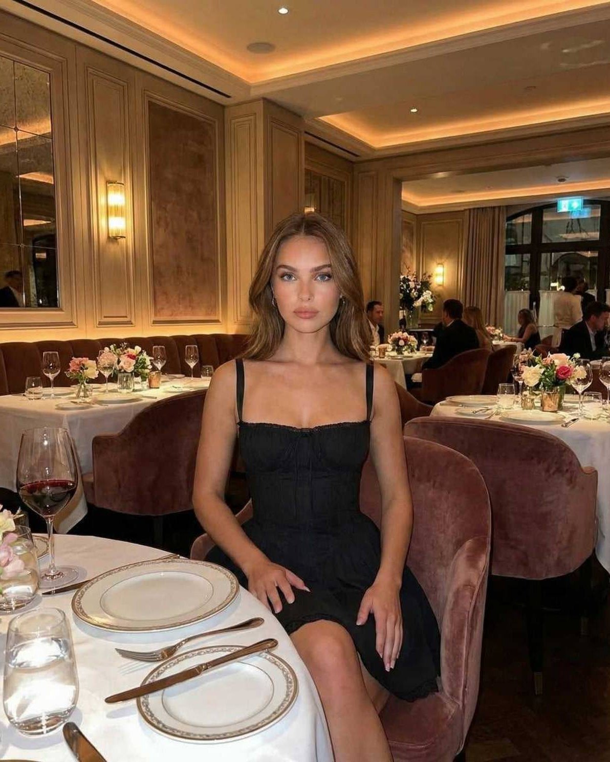 Vesper Mini Dress – Black corset style mini dress with lace trim worn in a dining setting, showcasing sophistication and elegance.